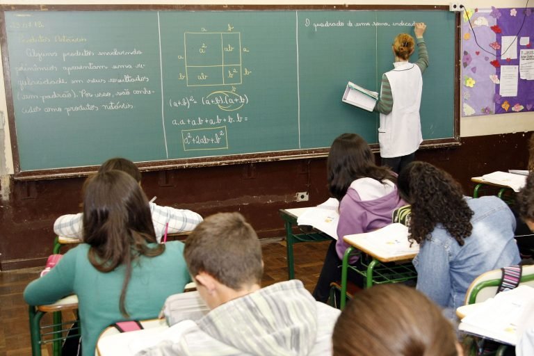 Professor escreve no quadro enquanto alunos copiam