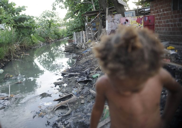 Uma criança caminha numa favela com esgoto a céu aberto