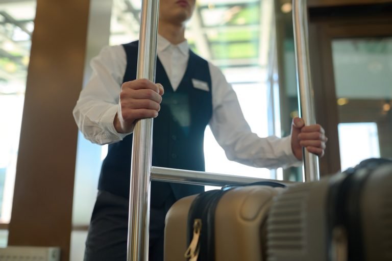 Mensageiro empurra carrinho com malas em hotel, hotelaria, turismo