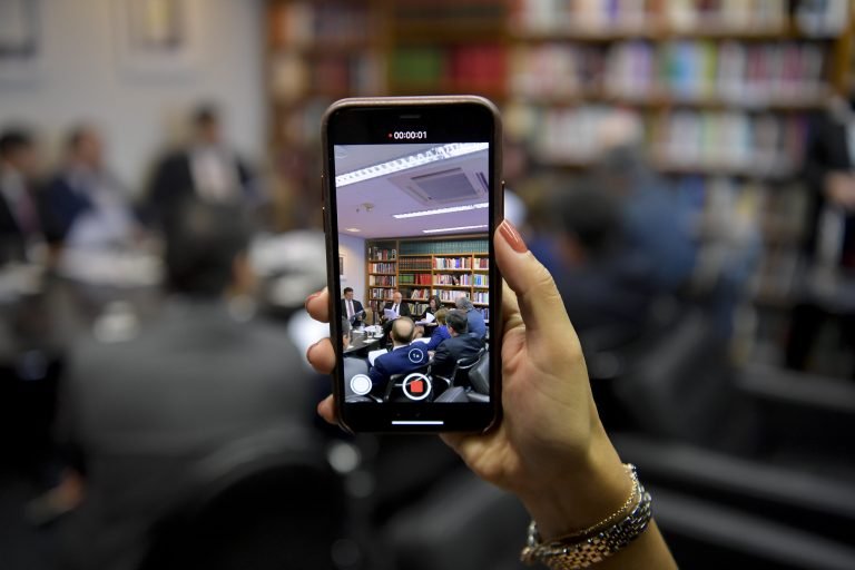 A mão de uma mulher segurando um celular e gravando uma reunião
